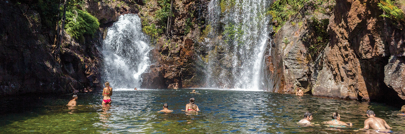 People hanging out in water below a large waterfall.
