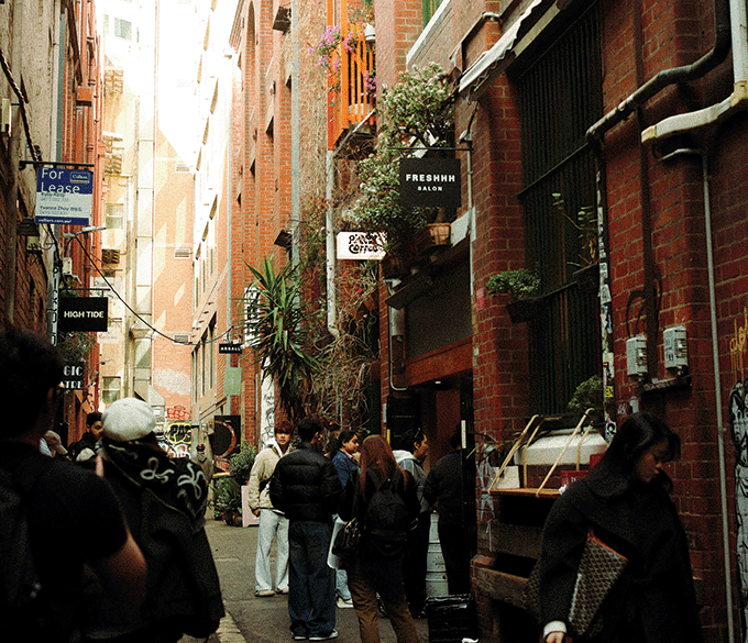 People explore an alley with shops between two brick buildings.