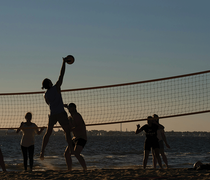 Group playing beach volleyball in low afternoon light.