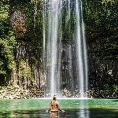 The back of woman as she wades toward a waterfall.
