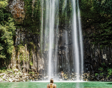 The back of woman as she wades toward a waterfall.