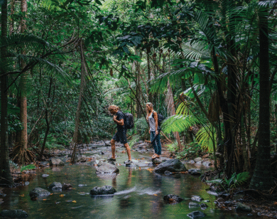 A man and a woman use rocks to cross a stream in Queensland rainforest.