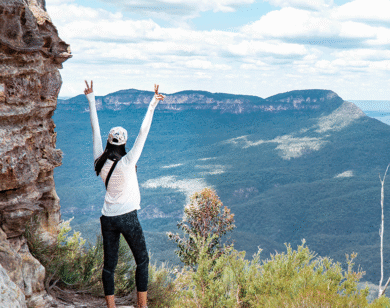 Woman overlooking a mountain range holding up two peace signs.